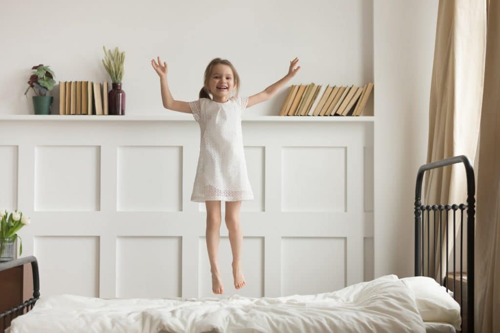 Happy funny child girl jumping on bed alone feeling joy