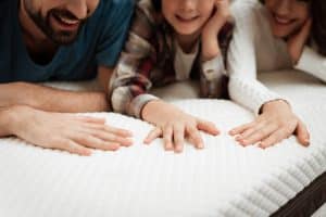 Young couple together with their young son test material of mattress for a touch.